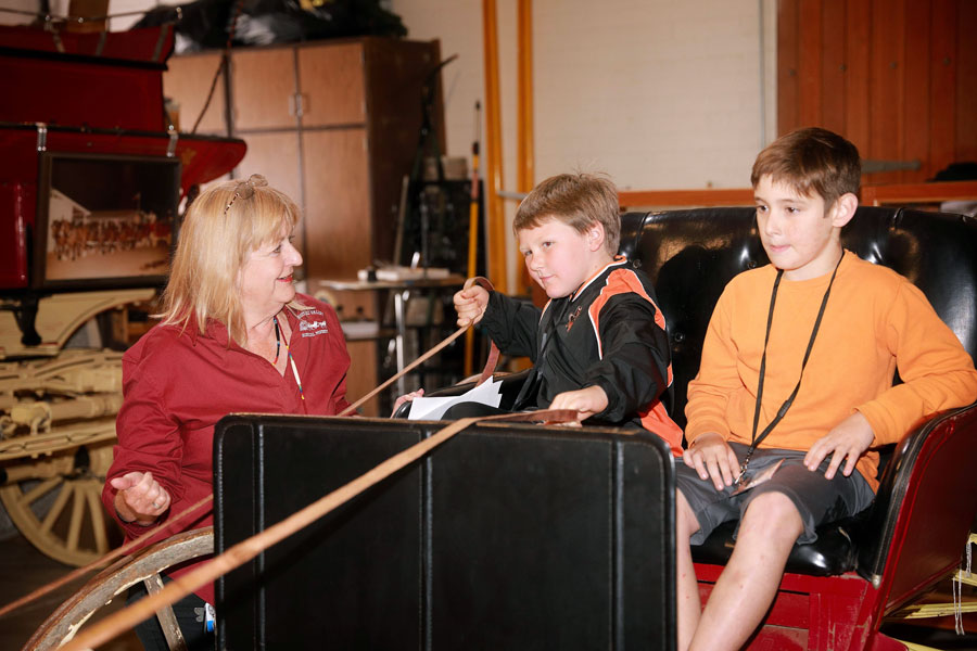 woman showing two boys how to steer a wagon using reins